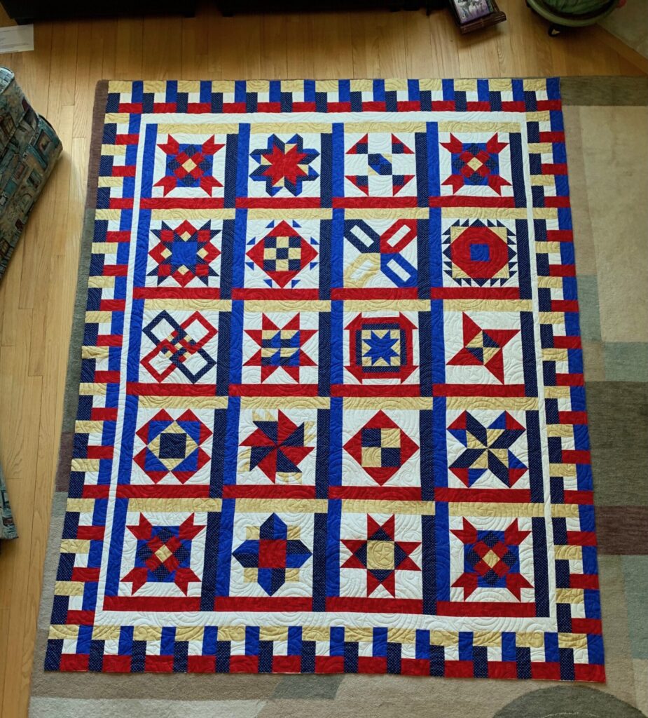 Patchwork quilt laid on the floor with red, white, blue star blocks and blue-gold-red striped borders.
