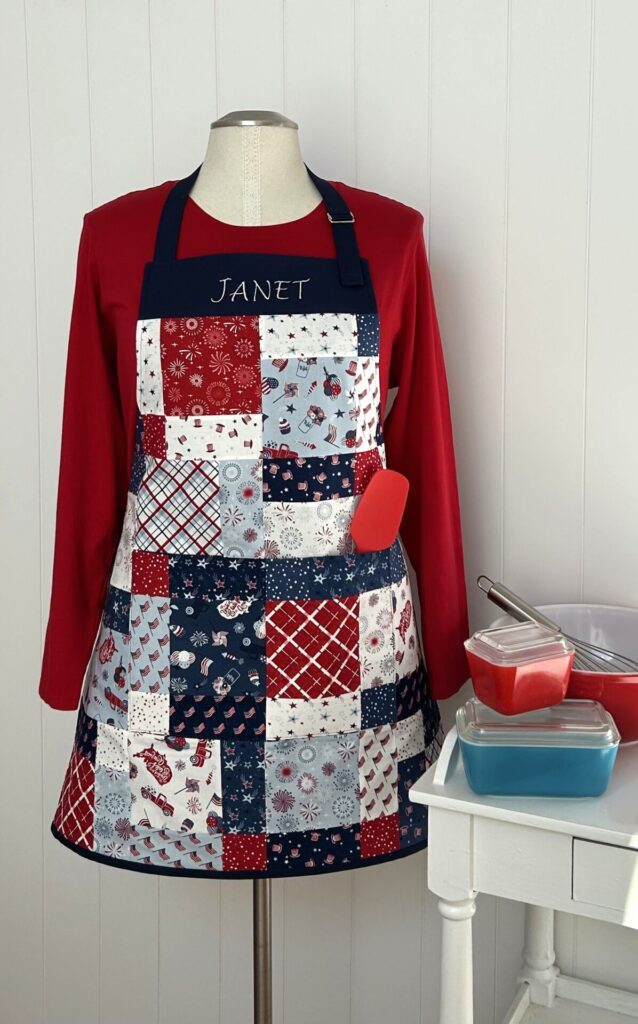 Mannequin wearing a patriotic patchwork apron with 'JANET' embroidered on the bib and a red spatula tucked in the pocket.