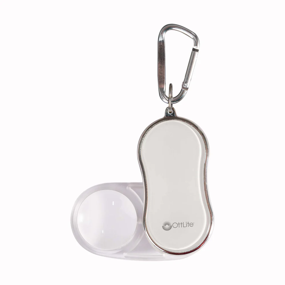 Portable magnifier with a white rounded body, metal edge, and a carabiner clip; OttLite logo on the front.