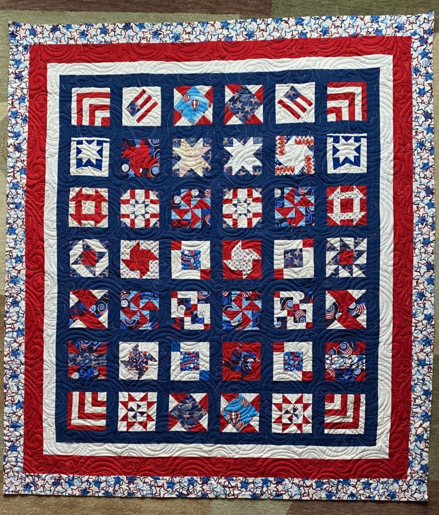 Patriotic quilt featuring navy blue inner blocks, red borders, and white-and-red star-patterned outer border with quilted spirals throughout.