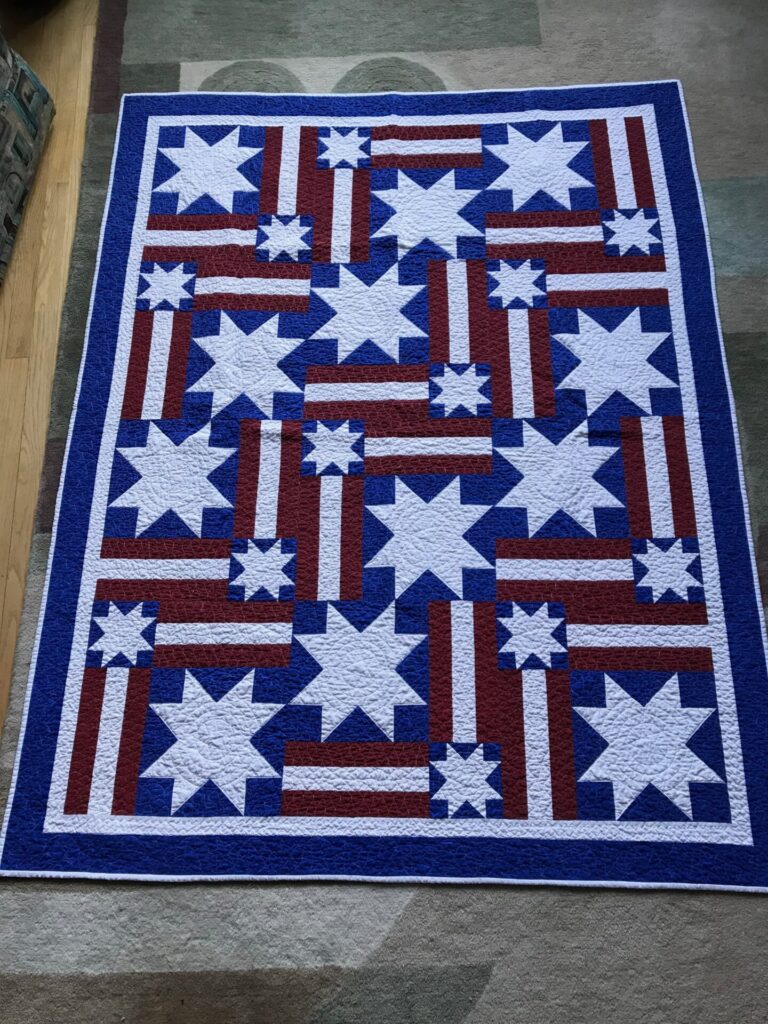 Blue, red, and white patriotic quilt with star blocks and striped panels on a blue border.