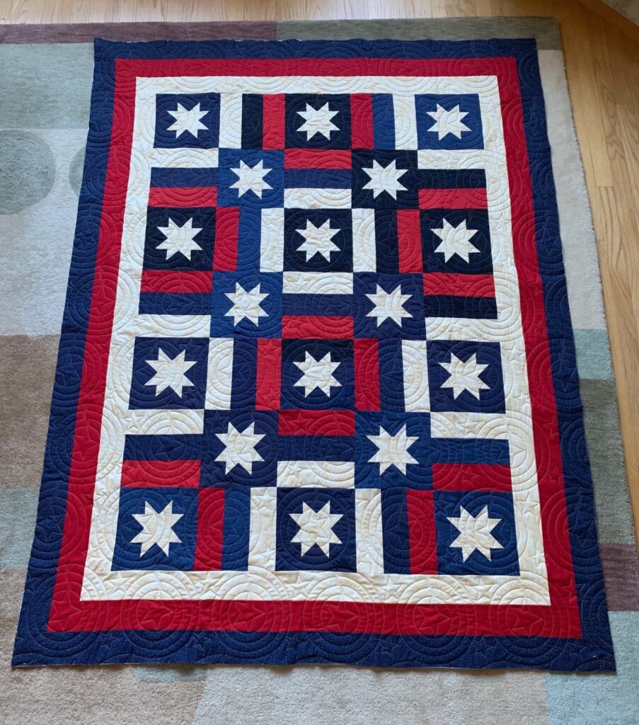 Patriotic patchwork quilt in red, white, and blue with white starburst blocks and curved quilting.