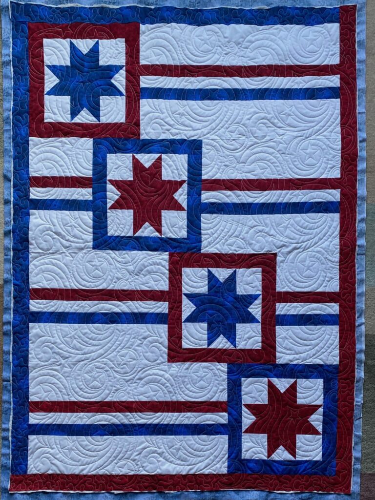 Patriotic quilt with blue star blocks, red and white stripes, and swirled quilting patterns in red, white, and blue border.