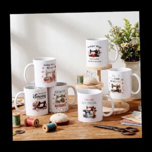 White mugs with sewing-themed designs and quotes on a wooden table, surrounded by thread spools, pins, scissors, and a bouquet of flowers.