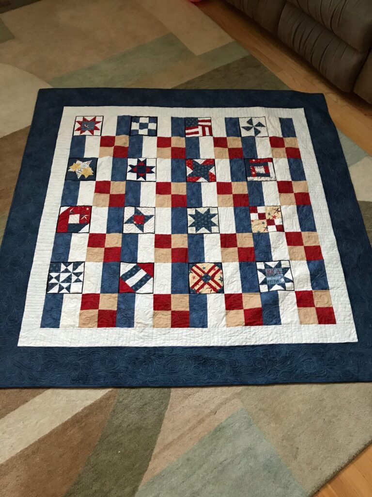 Patriotic patchwork quilt spread on the floor, featuring red, white, and blue squares and star blocks with a dark blue border.