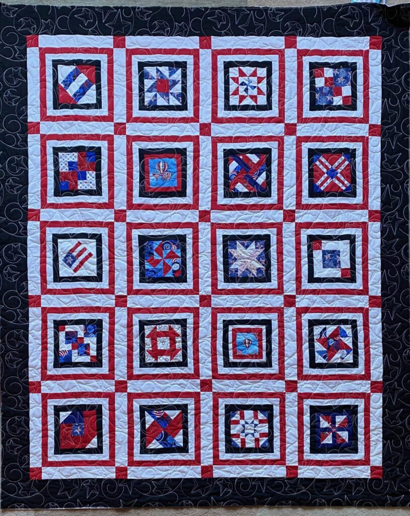 Patriotic quilt in a 4x4 grid of square blocks with red and white framing, black inner borders, and assorted blue-red-white centers featuring stars and stripes.